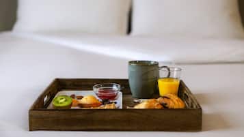 A breakfast tray with fruits, pastries, and drinks on a bed.