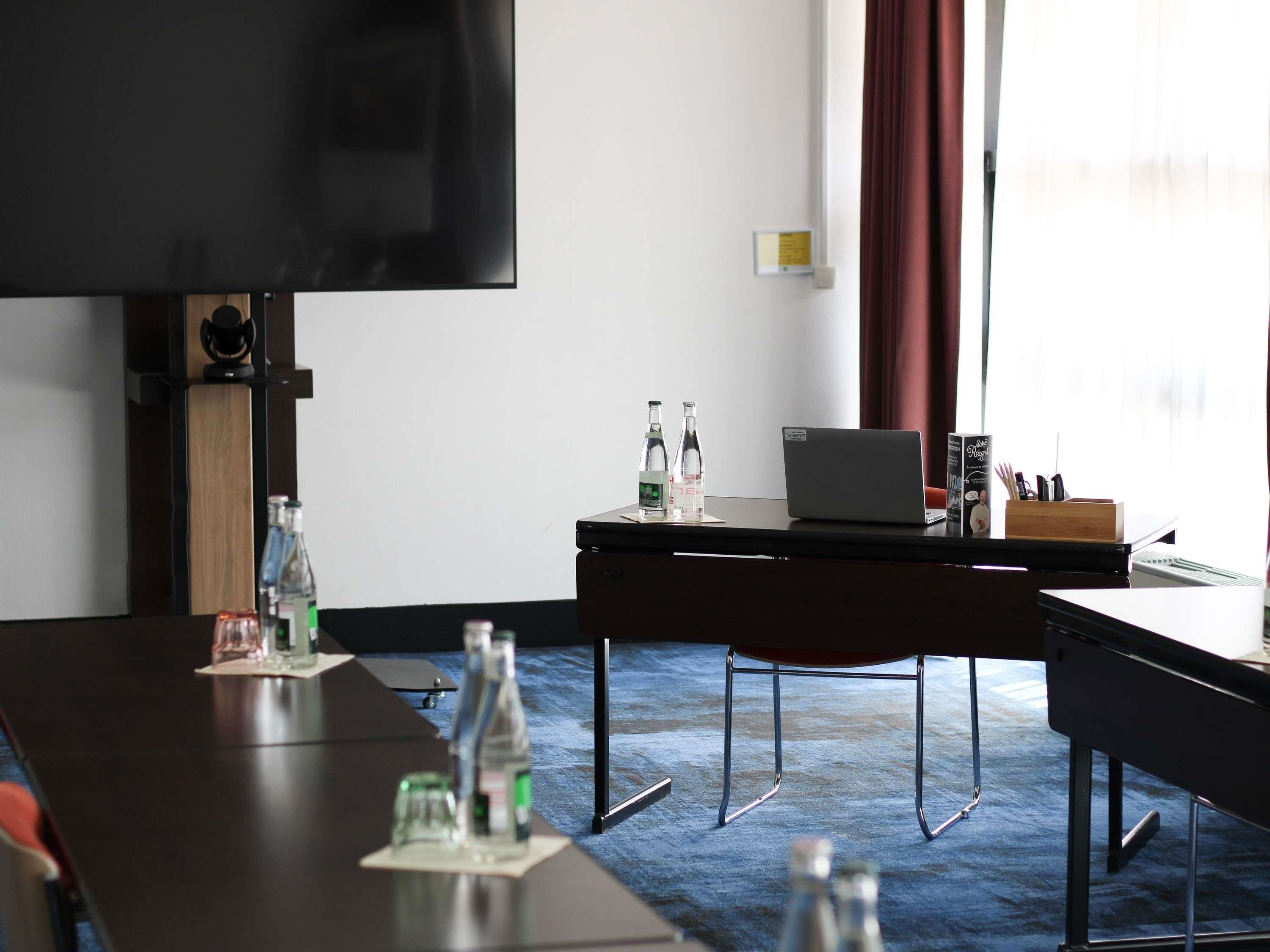 Une salle de conférence équipée d’un grand téléviseur à écran plat, d’un ordinateur portable et d’une table sur laquelle sont disposées des bouteilles d’eau.