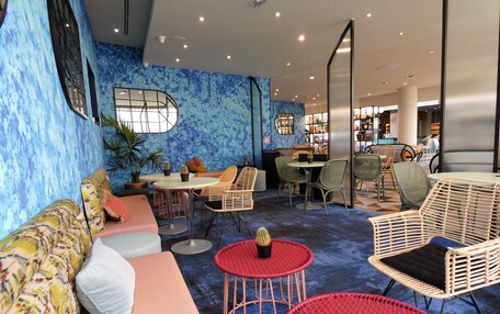 A modern lounge area with a blue textured wall, wicker furniture, and a central seating area with a round table.
