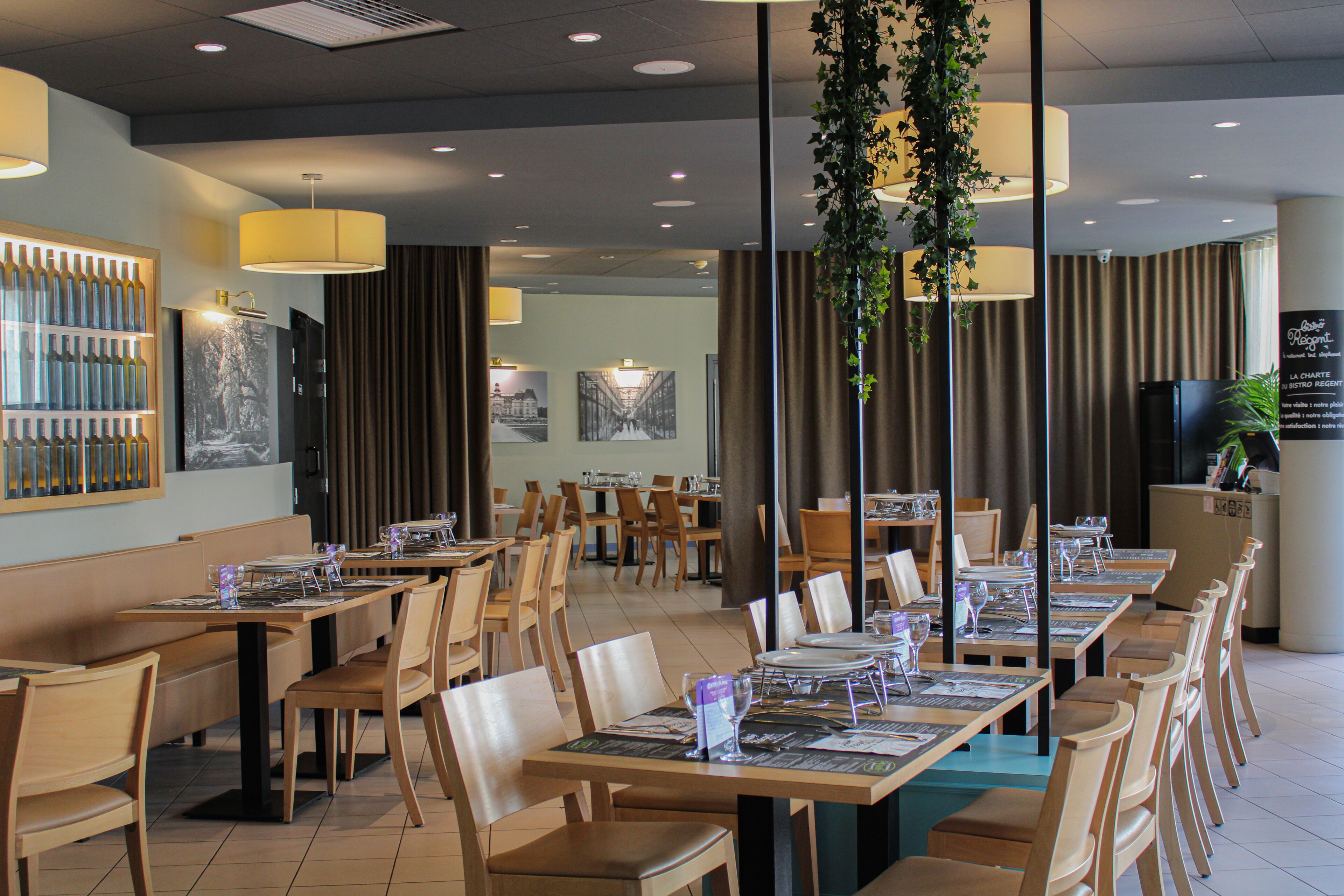 Un restaurant avec des tables et des chaises en bois, des plantes suspendues et un tableau affichant le menu.