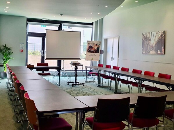 A conference room with long tables and red chairs, a whiteboard, and a poster on the wall.