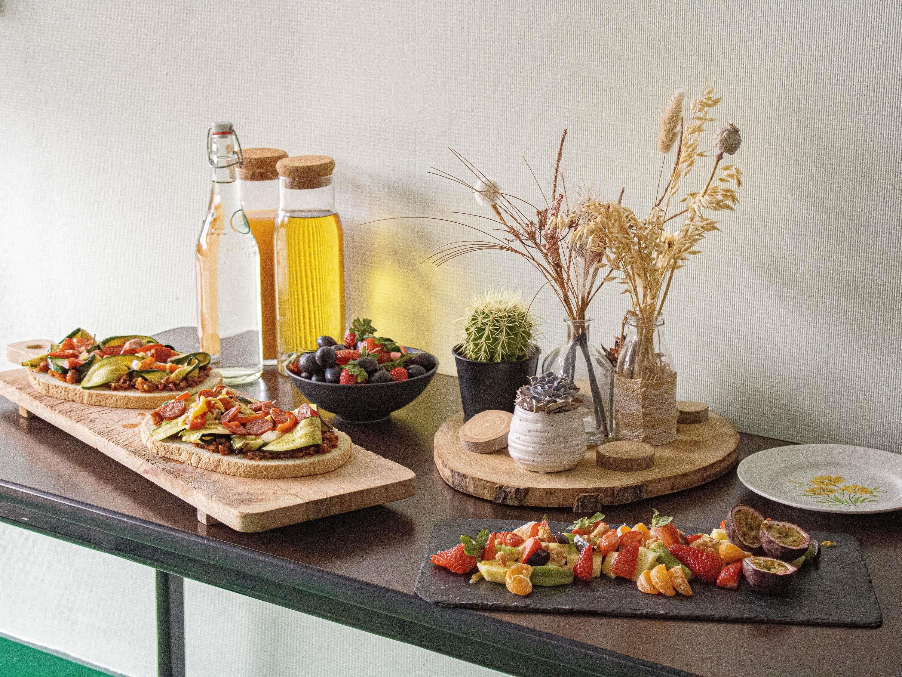 A table with food items, a bottle of oil, and decorative plants.