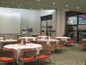 Ein Konferenzraum mit mehreren runden Tischen, Stühlen und einer Projektionsleinwand.
