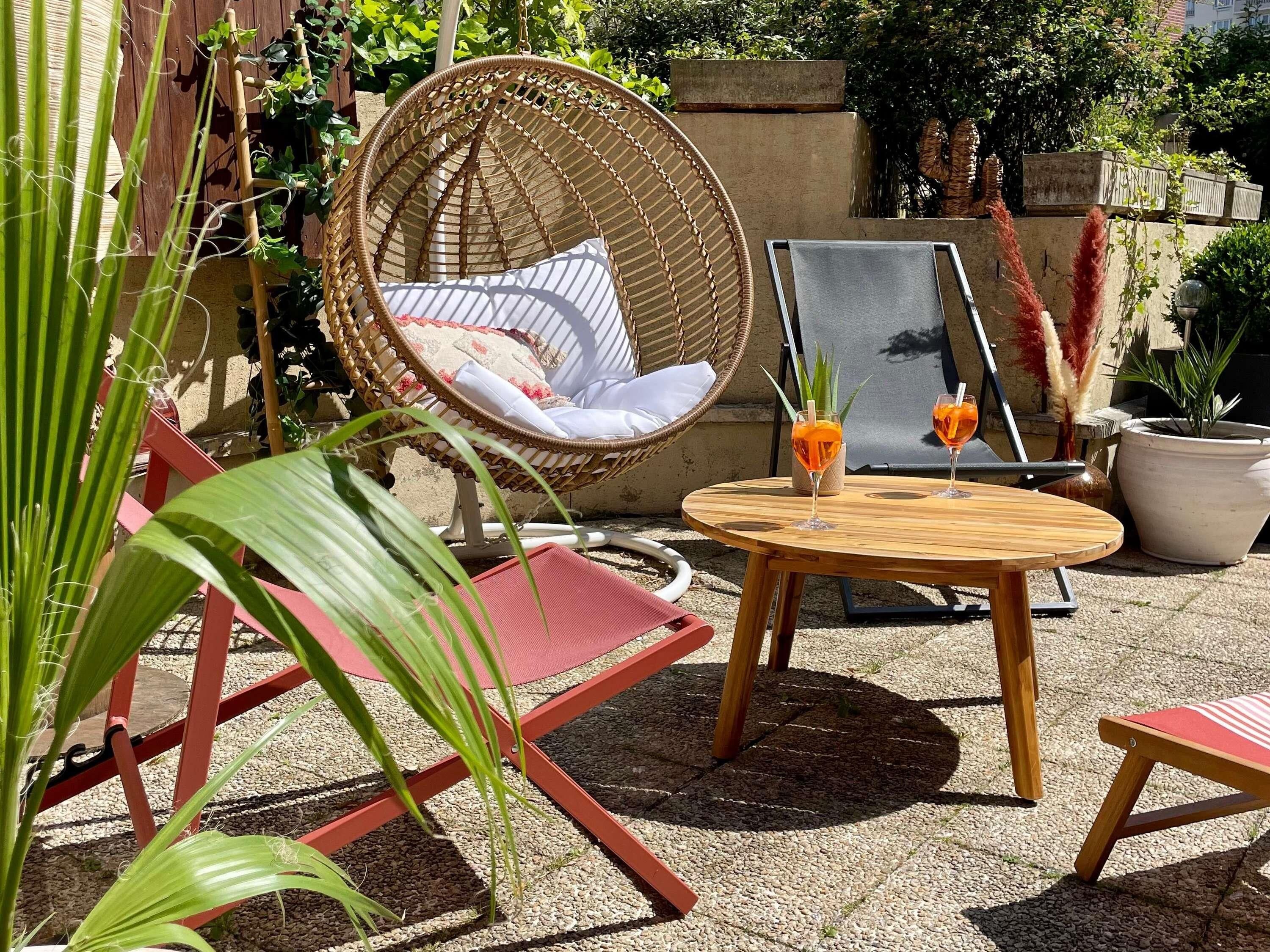 A wicker chair with cushions, a round wooden table with two glasses of orange drink, and red chairs.