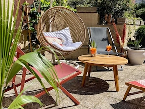 A wicker chair with cushions, a round wooden table with two glasses of orange drink, and red chairs. - ibis Styles Evry Courcouronnes Hotel and Events (Évry-Courcouronnes)