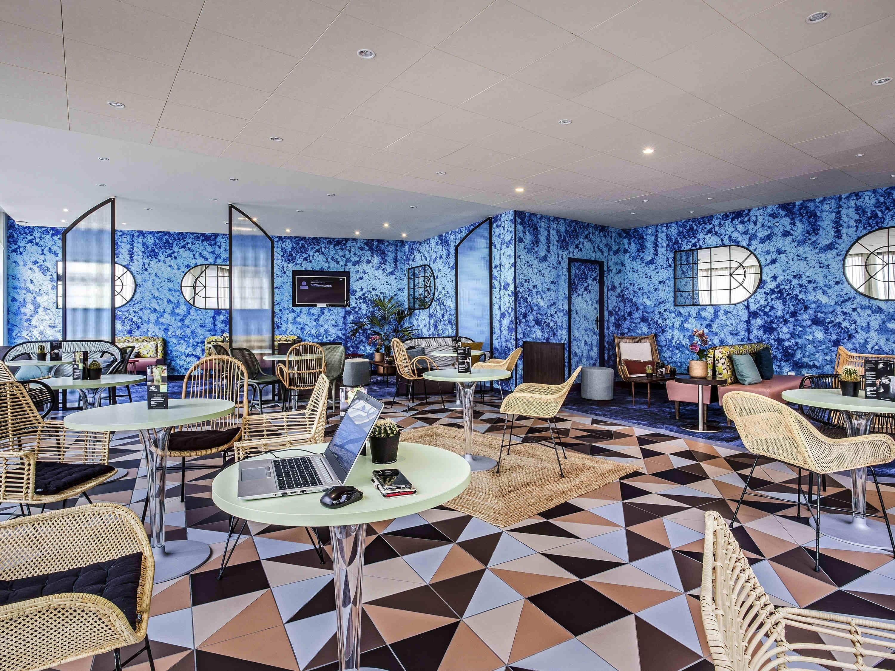 A modern lounge area with round tables, wicker chairs, and a patterned floor.