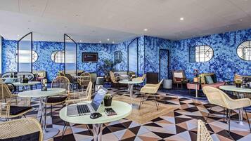 A modern lounge area with round tables, wicker chairs, and a patterned floor.