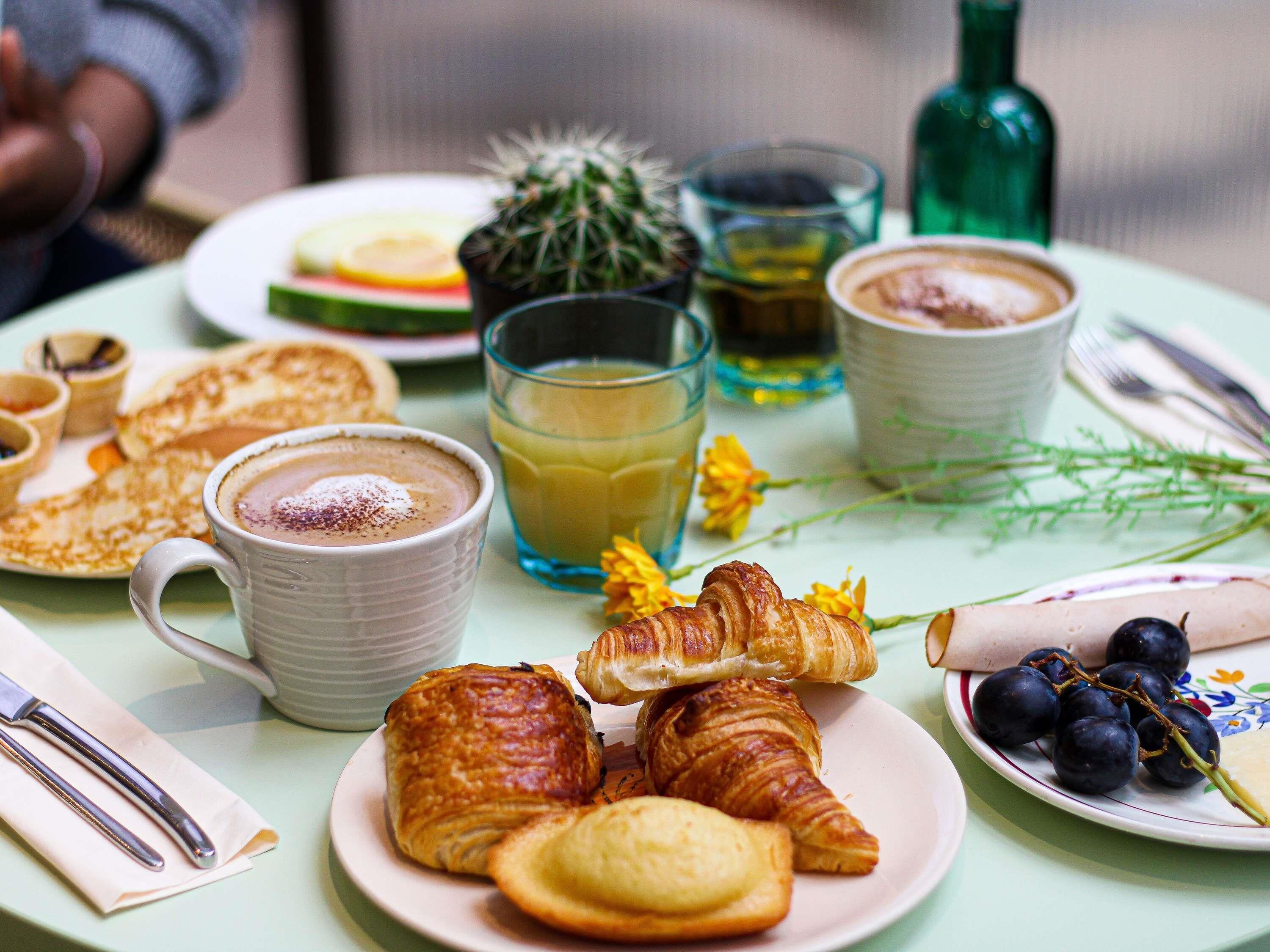 Une table dressée avec des croissants, une assiette de raisins, un verre de jus de fruits, une tasse de café et un petit cactus.