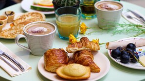 A table set with croissants, a plate of grapes, a glass of juice, a cup of coffee, and a small cactus.