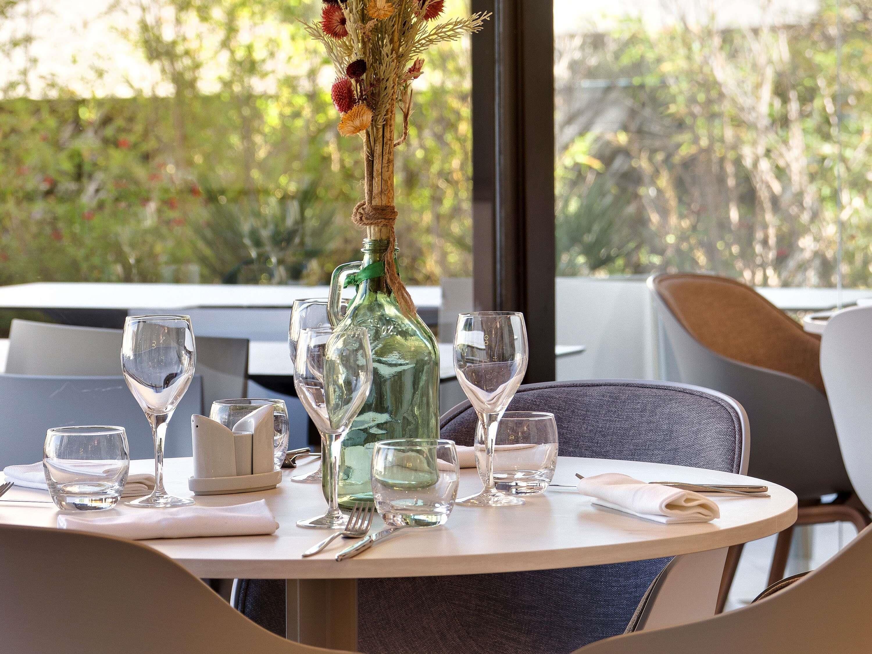 A dining table set with wine glasses, a bottle, and a vase with dried flowers.