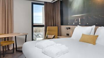 Una camera d'albergo con un letto grande, una scrivania, una sedia e vista sulla città attraverso una finestra.