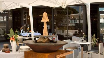 An outdoor seating area with a central fire feature, tables, chairs, and a white umbrella structure.