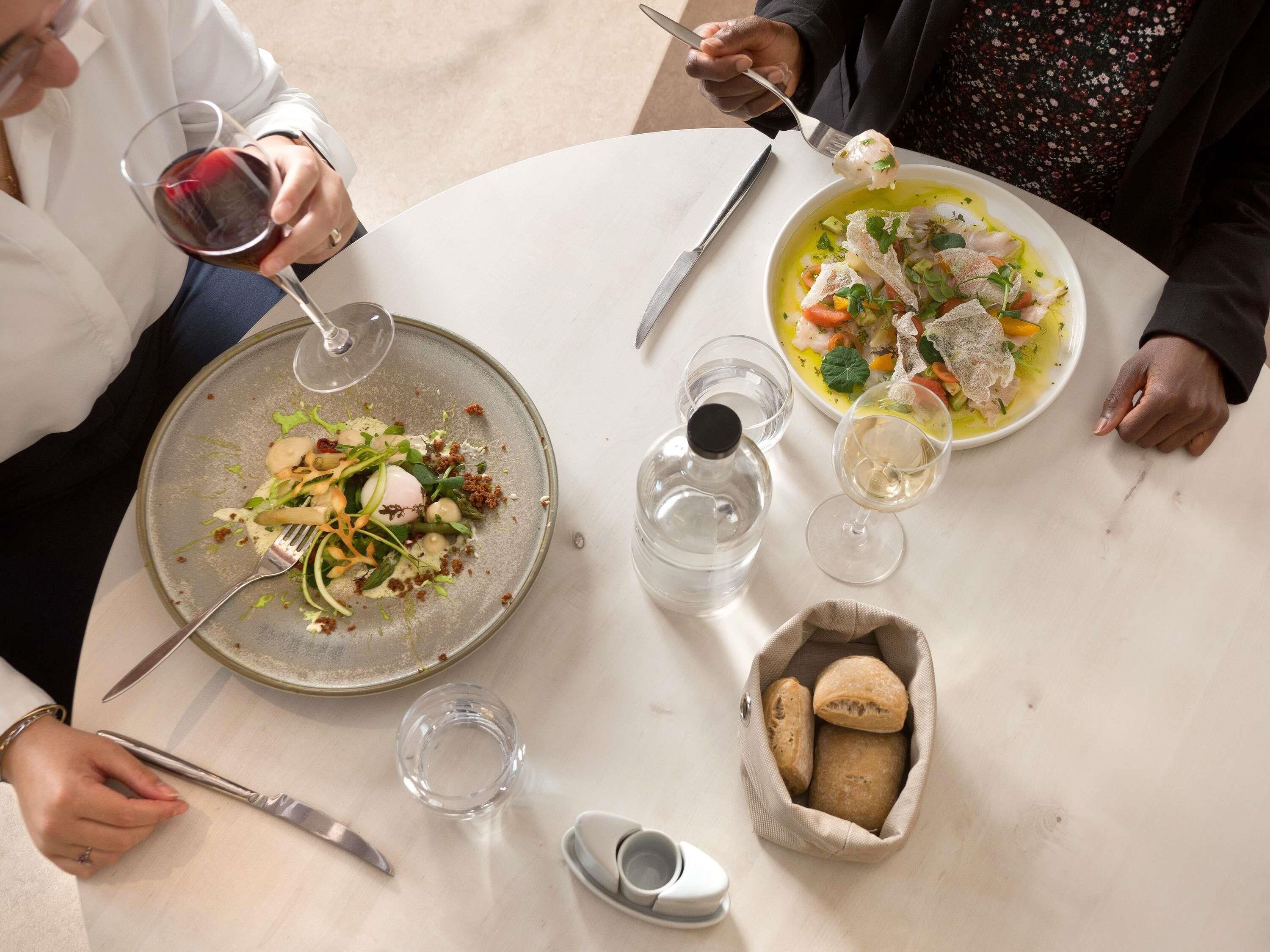 A dining table with plates of food, glasses of wine, and a bottle of water.