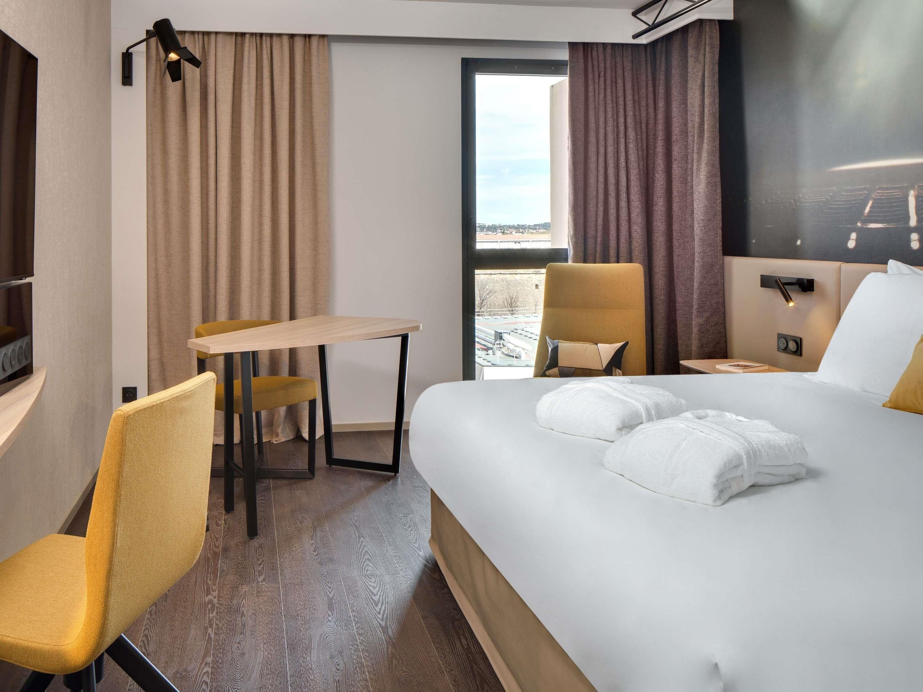 Ett hotellrum med en säng, ett skrivbord, en stol, en tv och ett fönster med utsikt.