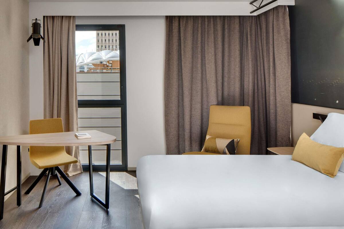 Habitación de hotel con cama, escritorio, silla y vista a un edificio a través de la ventana.