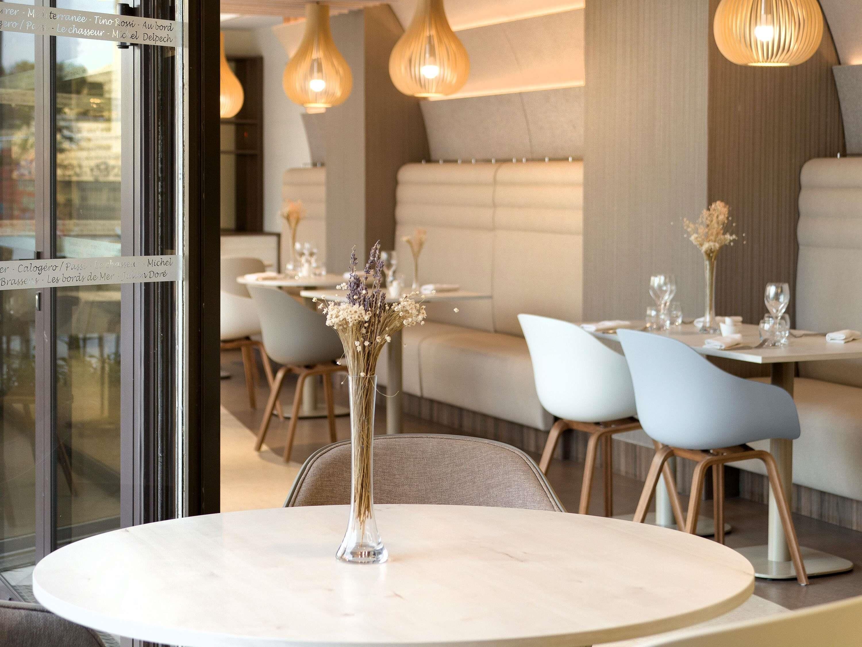 A restaurant interior with round tables, chairs, hanging pendant lights, and a glass partition with menu items.