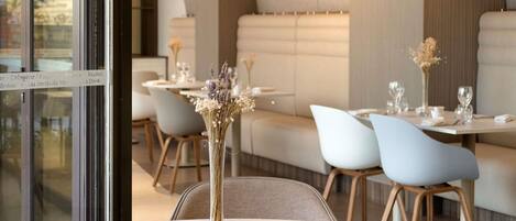 A restaurant interior with round tables, chairs, hanging pendant lights, and a glass partition with menu items.