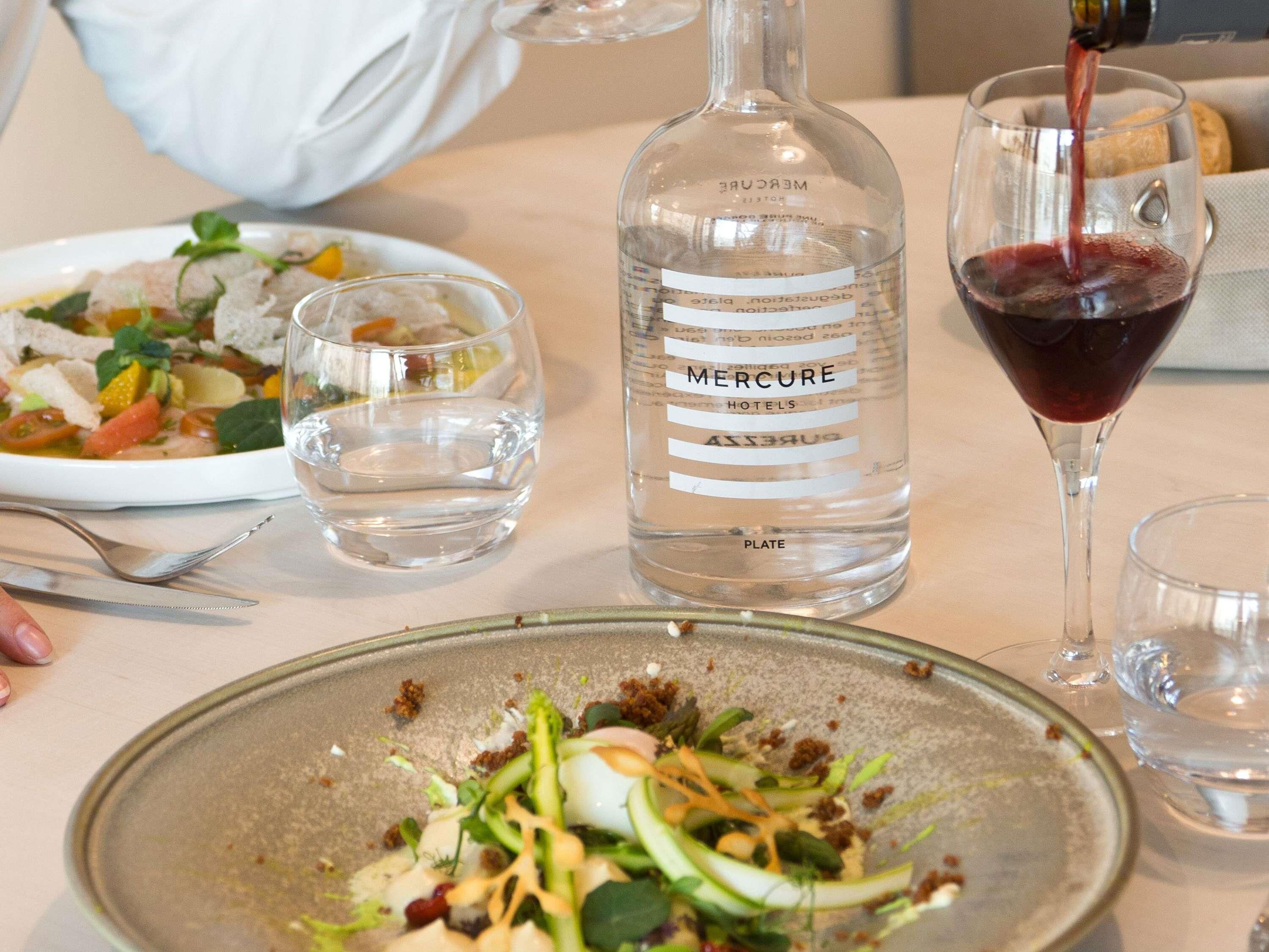 A dining table with a bottle of water, a wine glass, and plates of food.