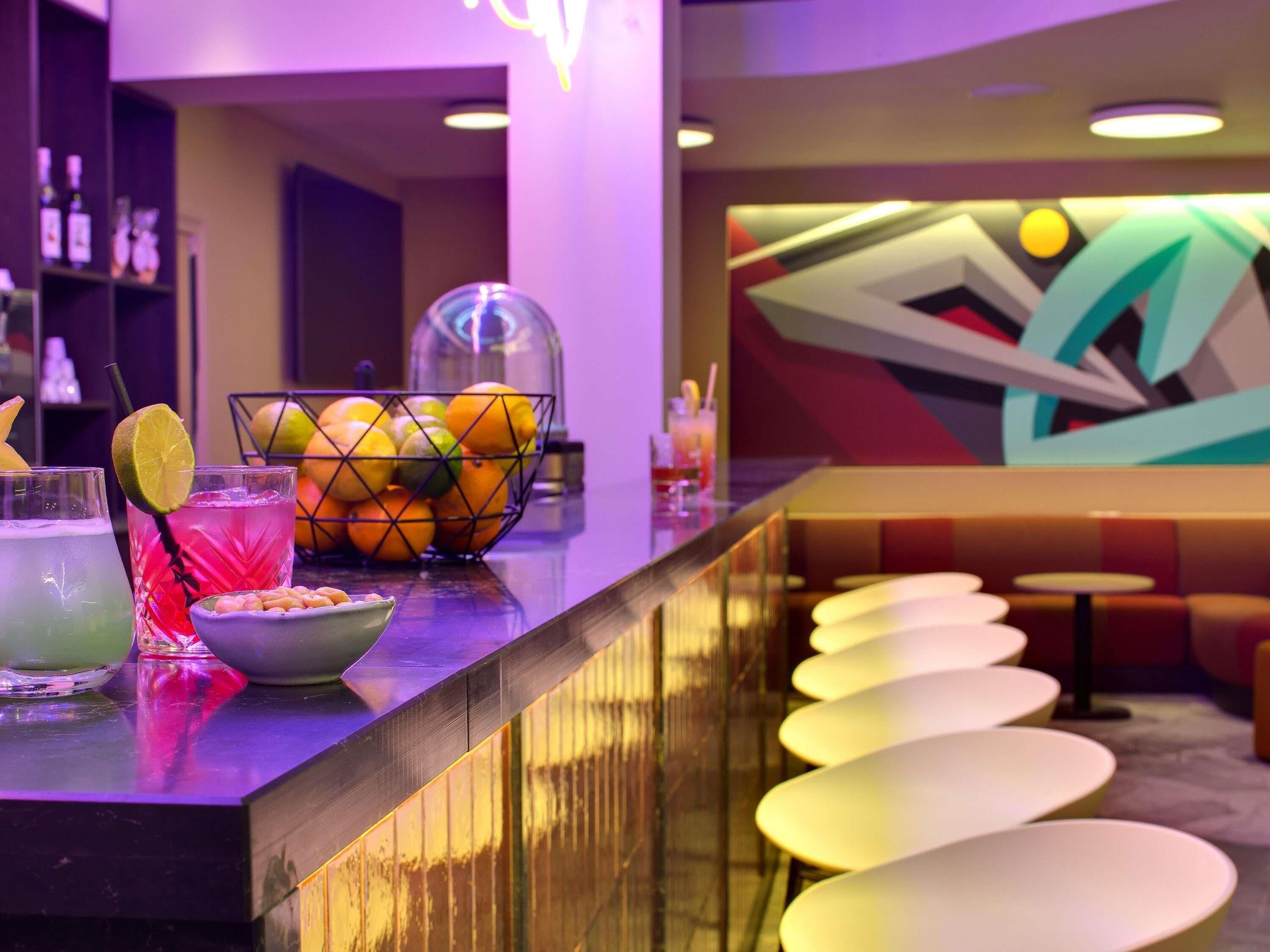 Uma área de bar com uma cesta de frutas, copos e um letreiro de neon.