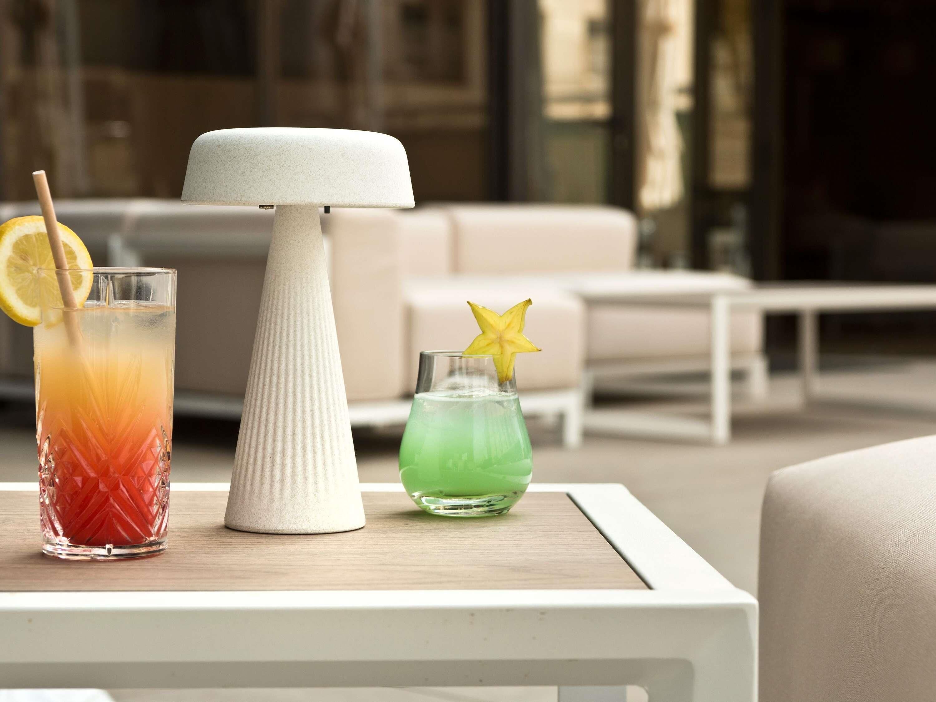 A table with two drinks, one with a lemon slice and one with a starfruit, and a white vase.