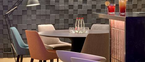 A modern dining area with a round table, chairs, a bar counter, and a wall with a geometric pattern.