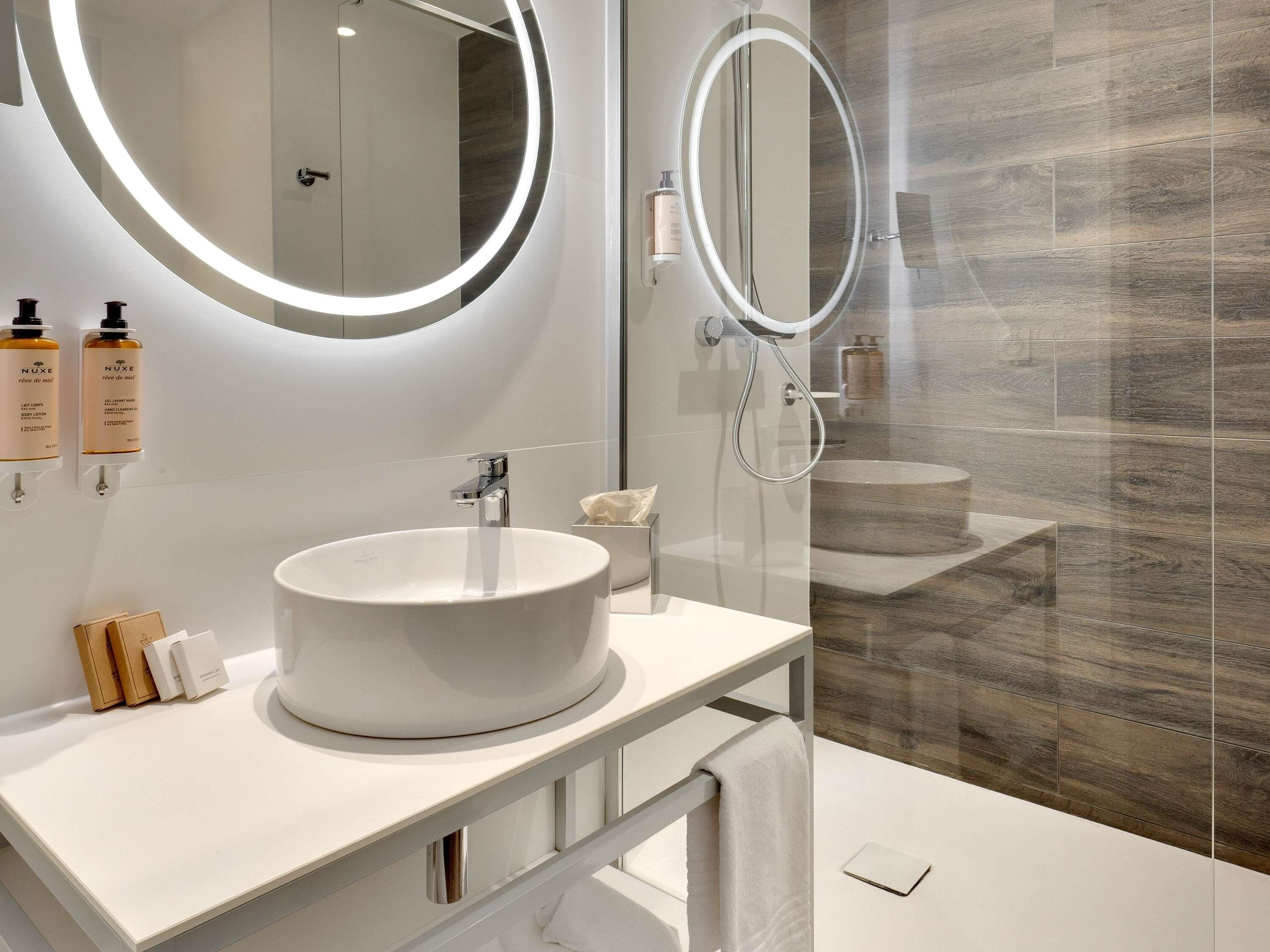 A modern bathroom with a round mirror, a white sink, and a glass shower enclosure.