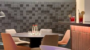 A modern dining area with a round table, cushioned chairs, and a bar with glasses and bottles.