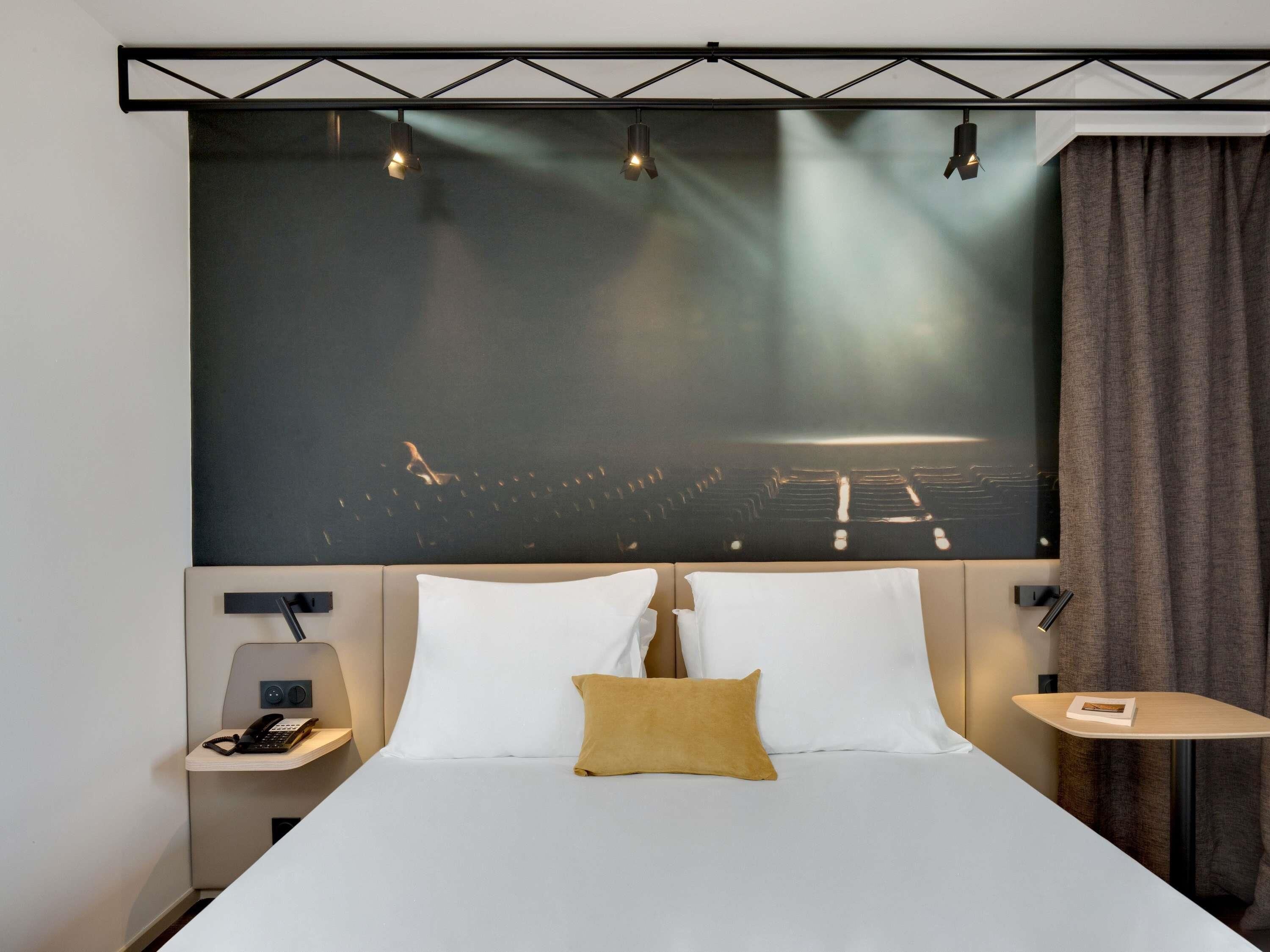 A hotel room with a large bed, two bedside tables, a nightstand, a wall-mounted TV, and a curtain.