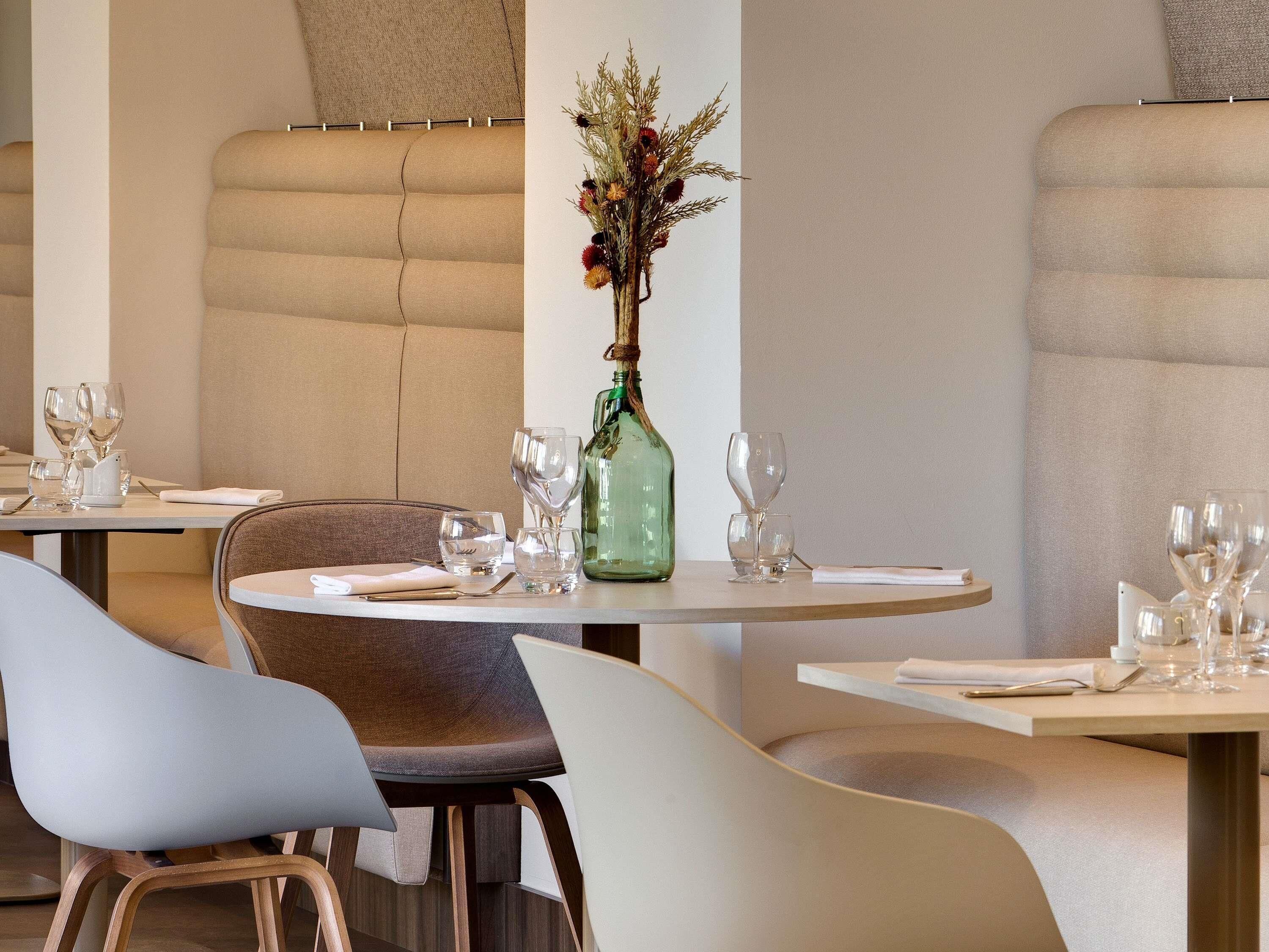 L’intérieur d’un restaurant avec des tables rondes, des sièges rembourrés et un vase décoratif rempli de fleurs.