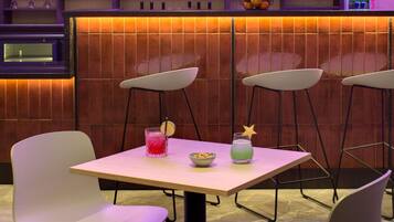 Zona de bar con salpicadero de azulejos, sillas blancas y una mesa con dos bebidas.
