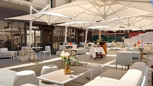 Un espace extérieur aménagé avec des tables, des chaises, des parasols et un vase de fleurs.