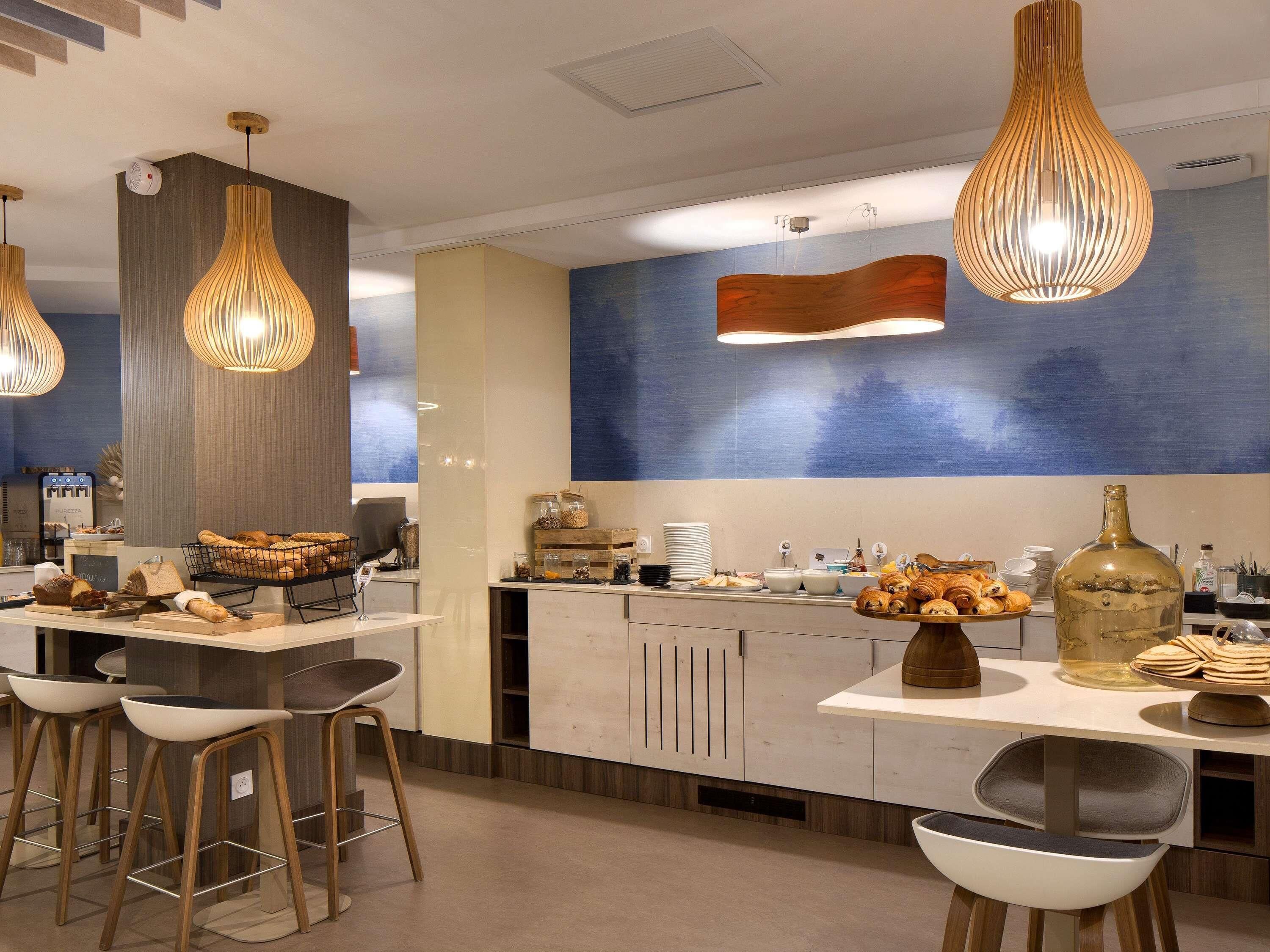 A modern kitchen with bar stools, a buffet counter with pastries, and pendant lighting.