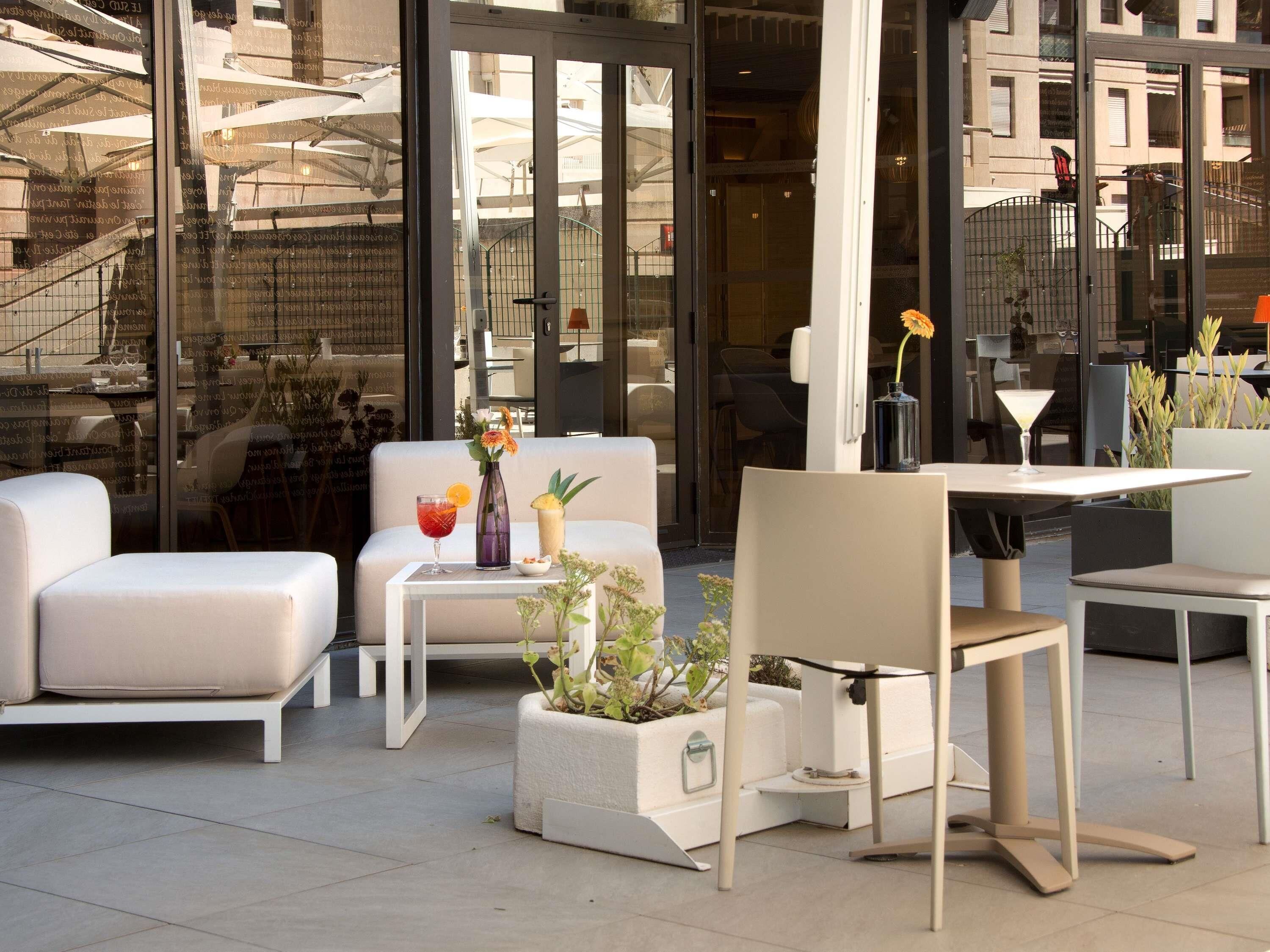 An outdoor seating area with white furniture, a glass door entrance, and a potted plant.