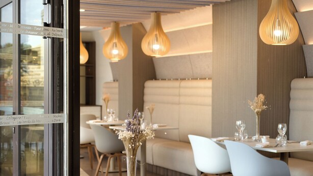 Un espace de restauration moderne avec des tables rondes, des chaises blanches et des luminaires suspendus.