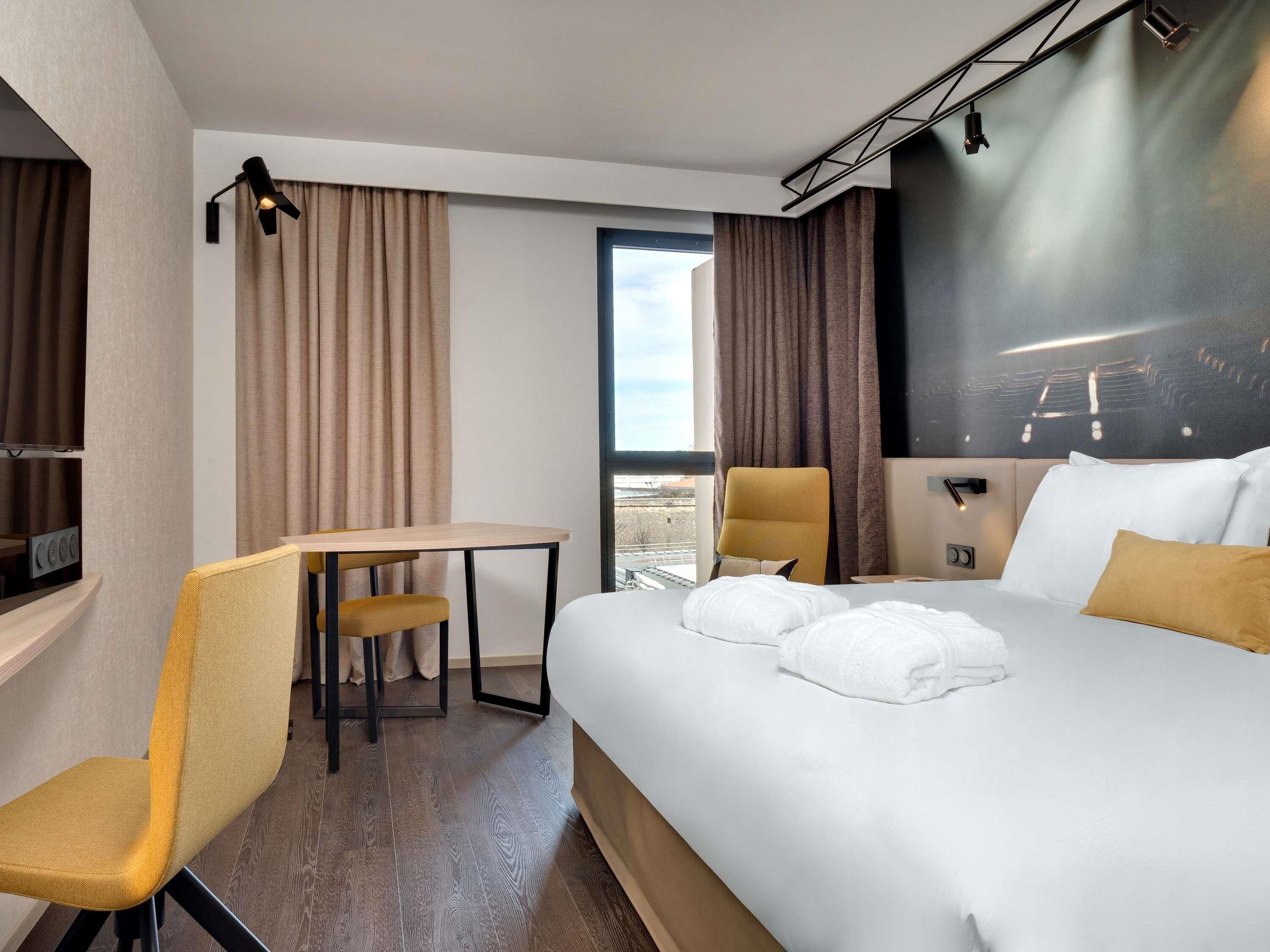A hotel room with a bed, a desk, a chair, a TV, and a large window.
