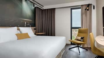 A hotel room with a large bed, a desk, a chair, and a view of the city.