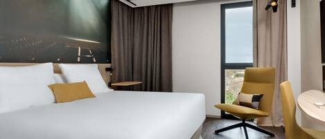 Habitación de hotel con una cama grande, un escritorio, una silla y vistas a la ciudad.