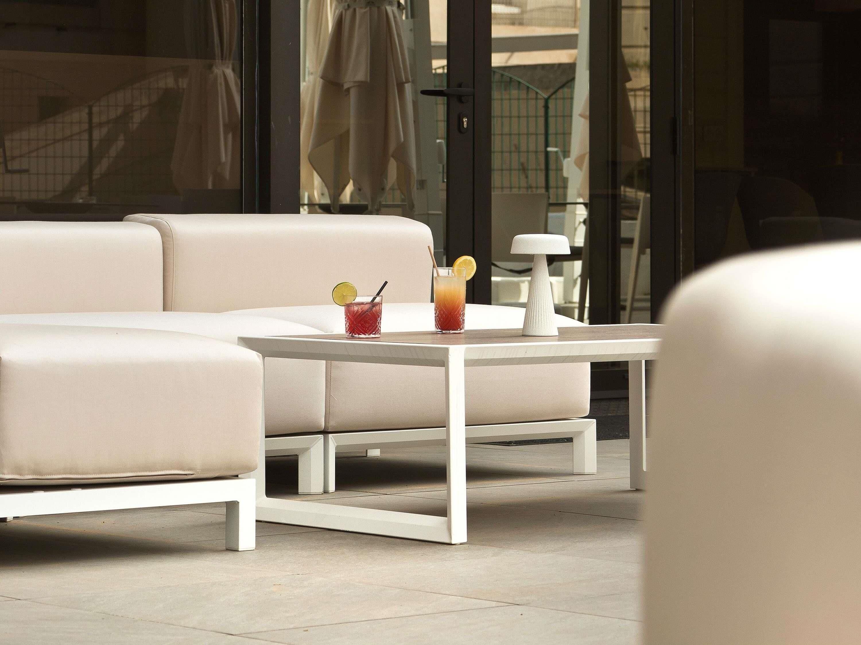 A modern outdoor seating area with a white sofa and table, a drink with a lemon slice, and a white lamp.