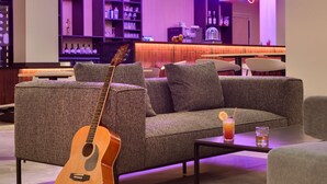 Un espace de détente moderne avec un canapé, une guitare et un bar doté d’étagères remplies de bouteilles.