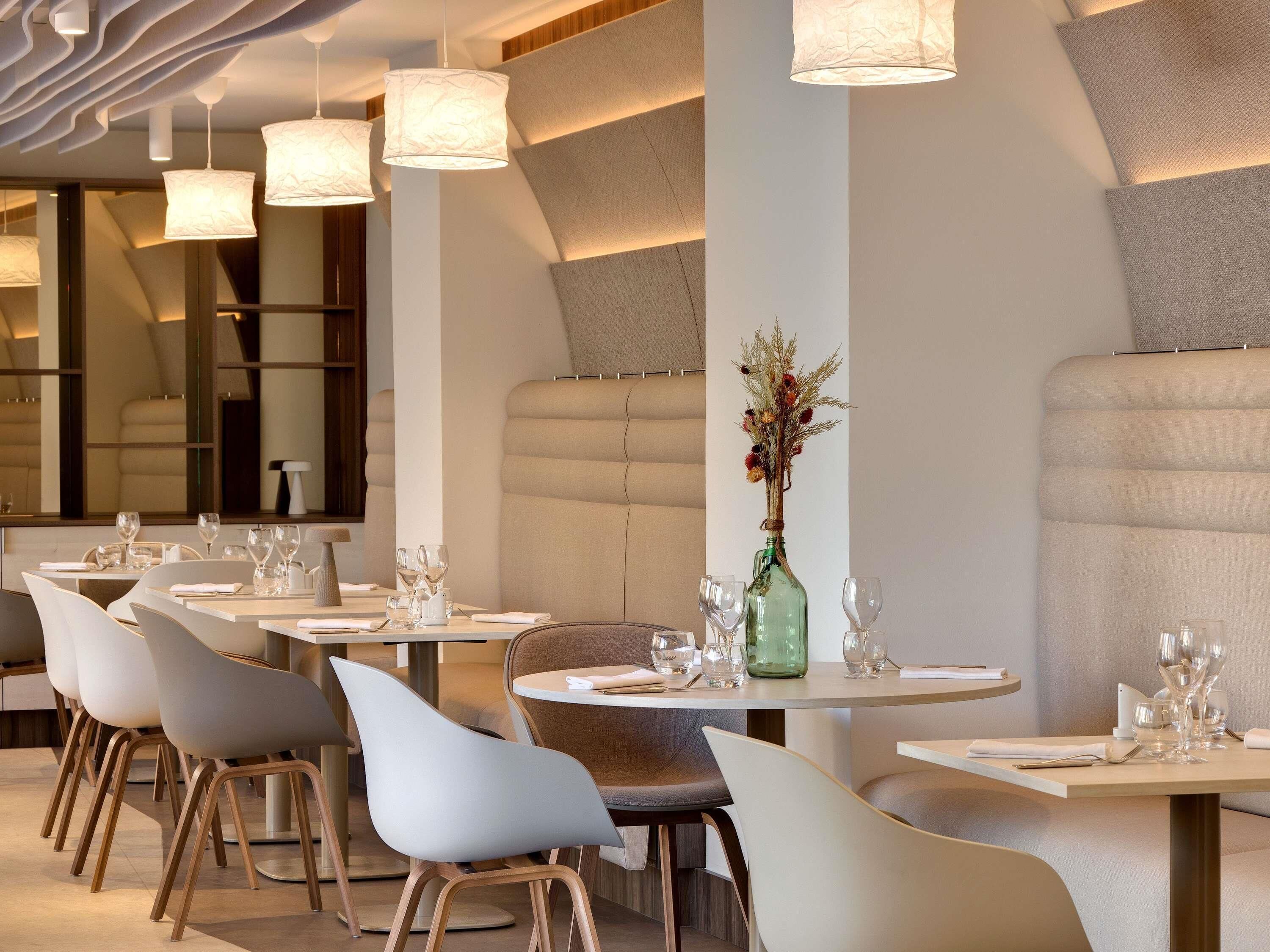 Un espace repas moderne avec des tables rondes, des sièges rembourrés et des luminaires suspendus.