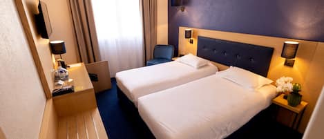 A hotel room with two beds, a desk, a chair, and a TV.