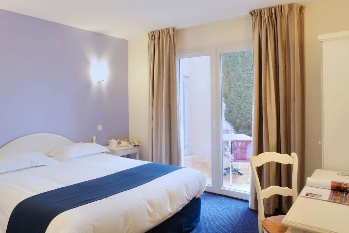 A hotel room with a bed, a desk, a chair, and a view of the outdoors.
