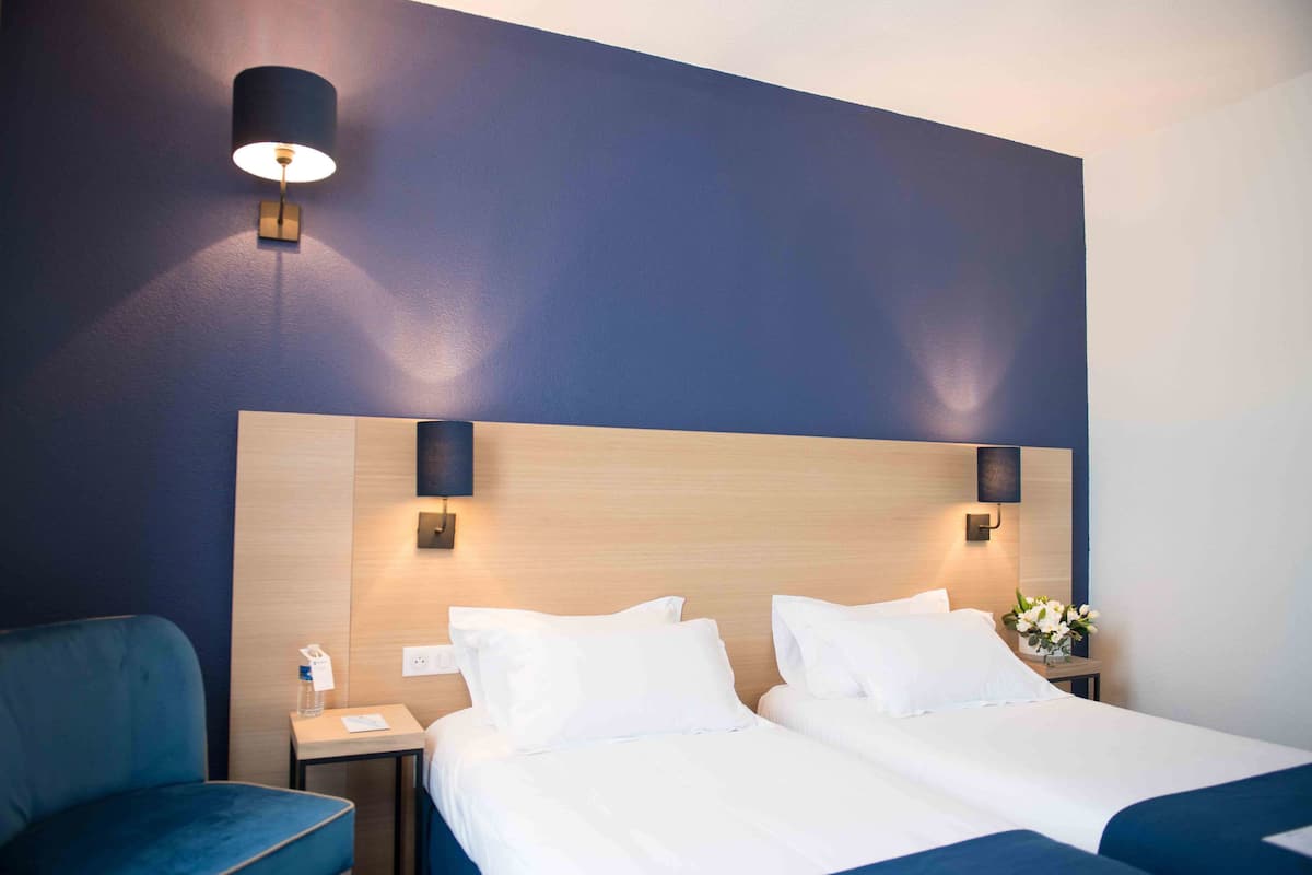 A hotel room with a large bed, two bedside tables, a chair, and a wall-mounted lamp.