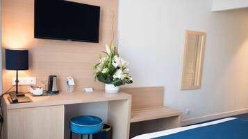 Habitación de hotel con cama, escritorio con lámpara, televisor y arreglo floral.