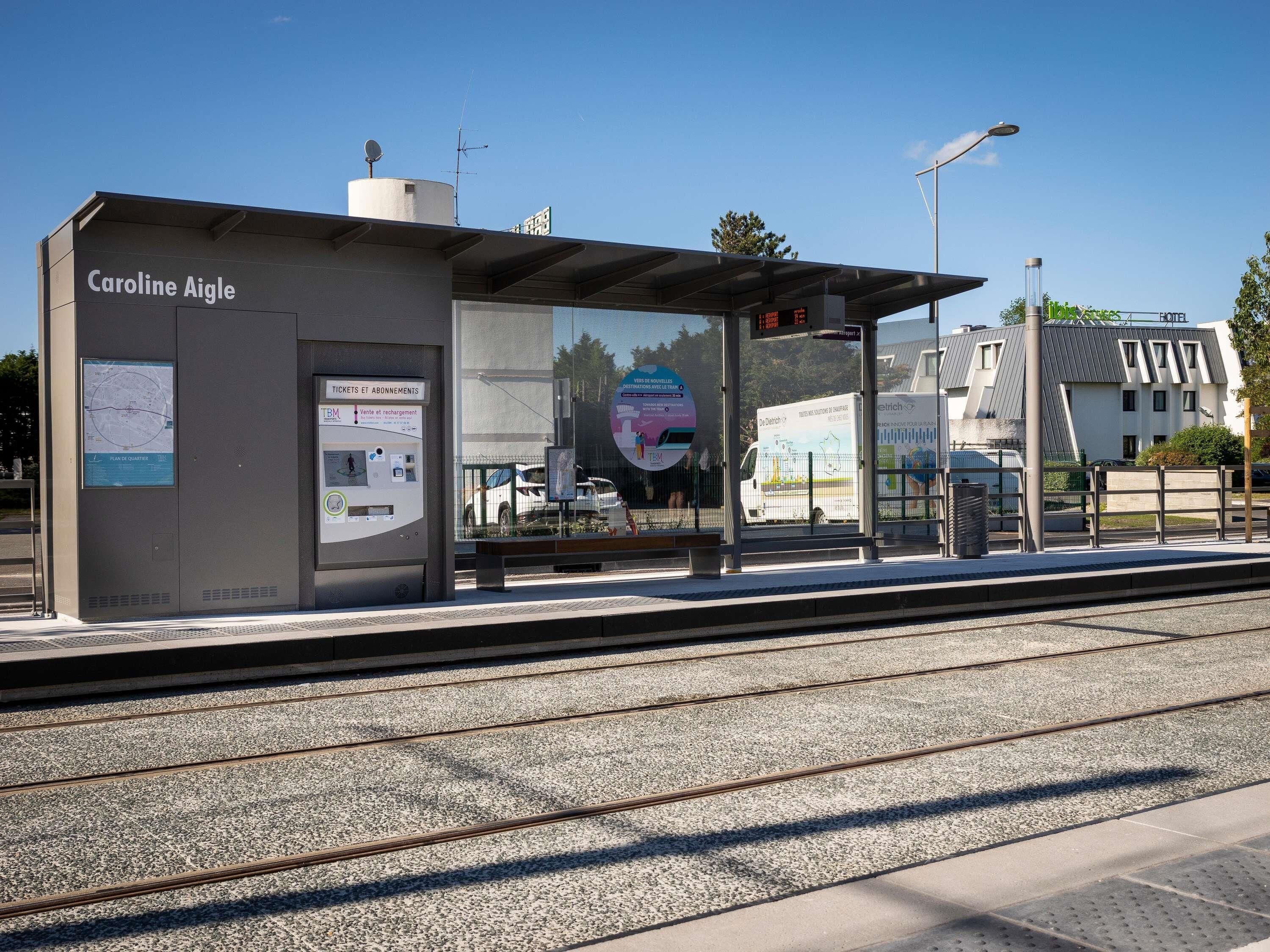 Un quai de gare doté d’un abri portant l’inscription « Caroline Aigle », d’un écran numérique et d’un plan.