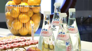Una mesa con botellas de Evian, un bol de naranjas y diversas frutas y quesos.