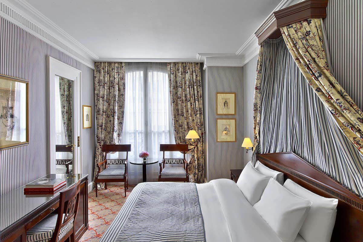 Ein Hotelzimmer mit einem großen Bett, zwei Sessel, einem kleinen Tisch mit einer Vase und einer Lampe.