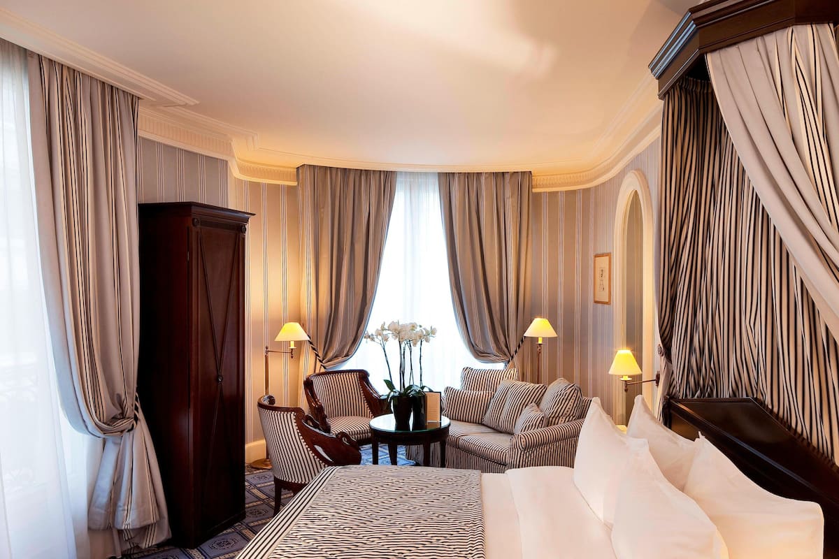 Ein Hotelzimmer mit einem großen Bett, einer Sitzecke mit Sofa und Sesseln, einem kleinen Tisch mit Blumenvase sowie einem Kleiderschrank.