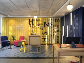 Un hall de hotel con mostrador de recepción, una computadora, un teléfono y una zona de estar con sillas.