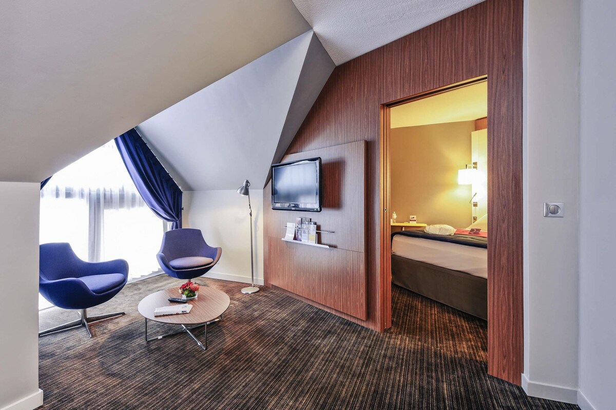 A hotel room with a TV, a bed, a desk, and a chair.